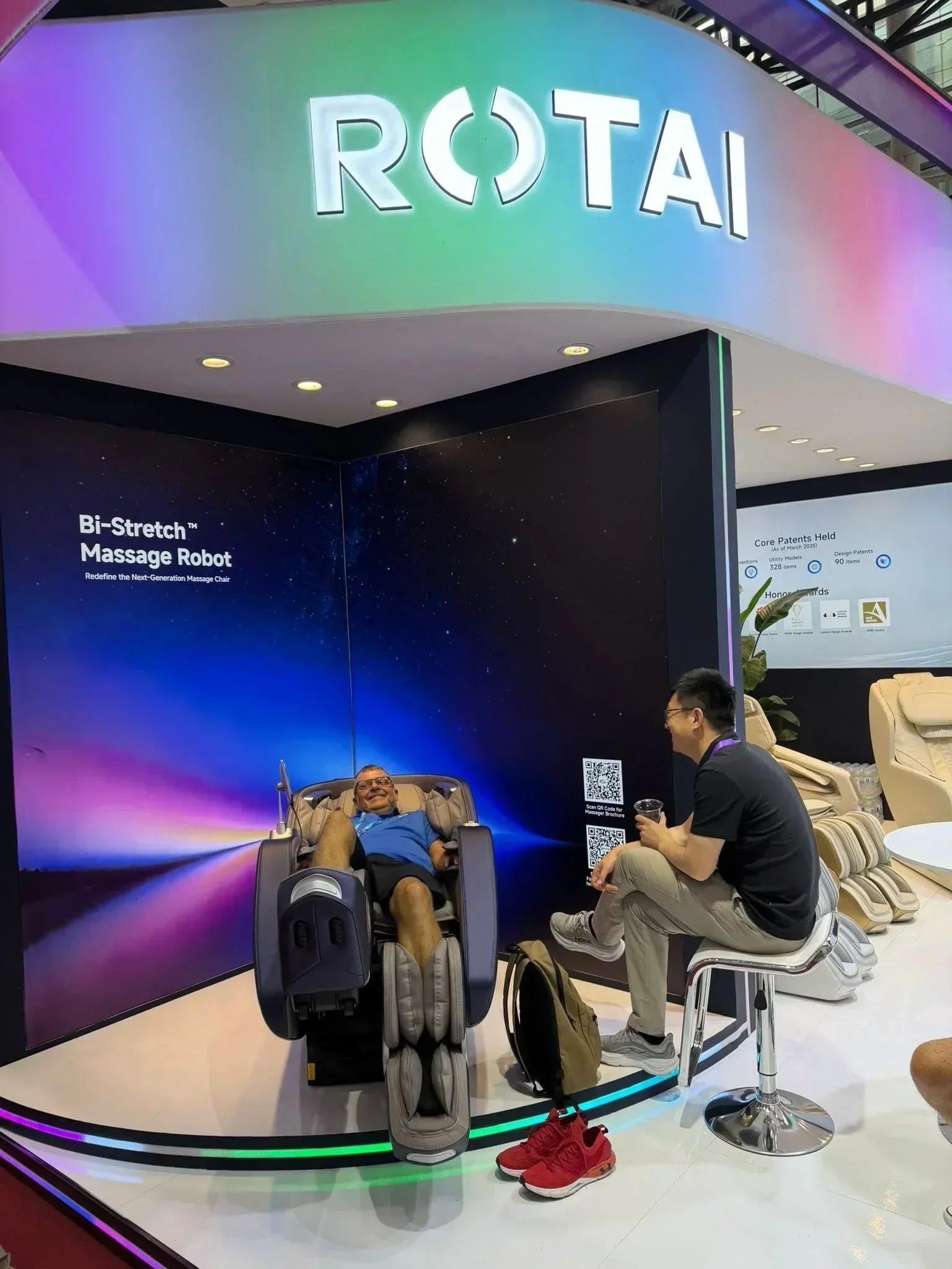 Man relaxing in a full body massage chair at an exhibition booth with modern lighting